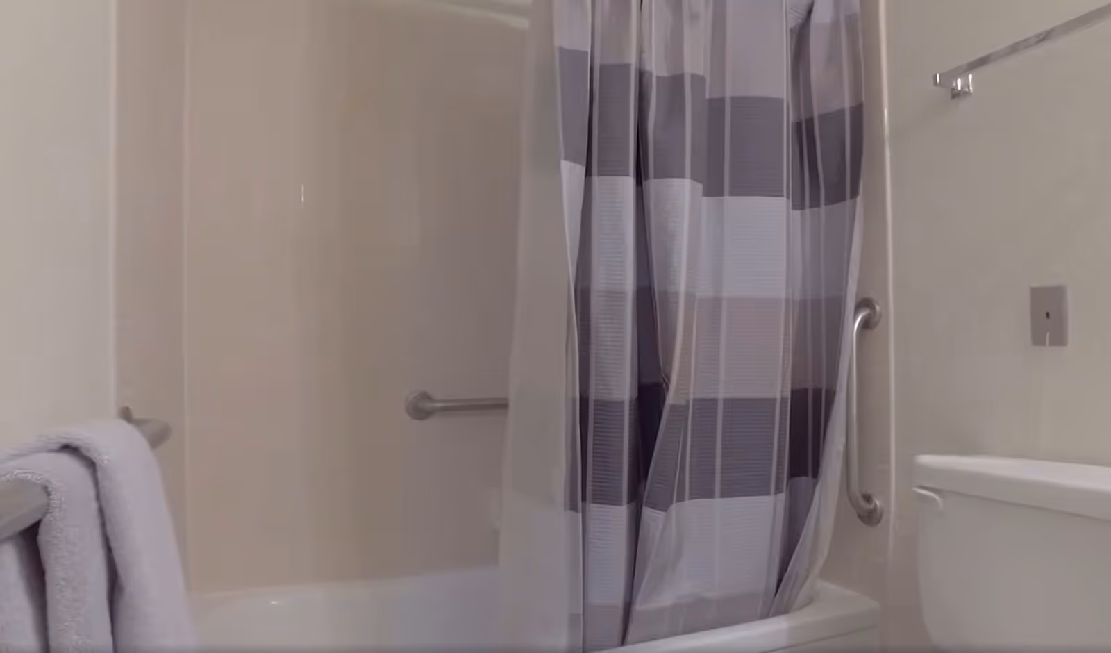 Bathroom with a bathtub and shower combination featuring a striped shower curtain. There are grab bars on the wall inside the bathtub area and next to the toilet. A towel is hanging on a towel bar to the left.