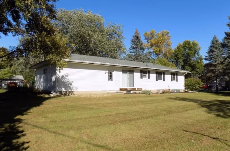 Single-story white building on a grassy lawn with trees and a clear blue sky.