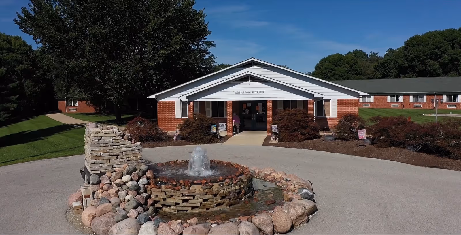 Front exterior of Cedar Ridge Health & Rehab Center with a circular driveway, stone fountain in the foreground, and the brick main entrance building.