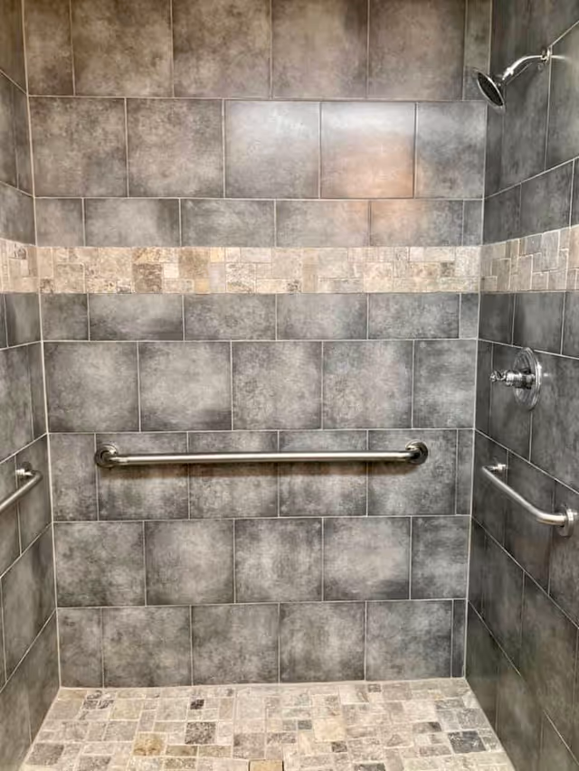 Tiled walk-in shower with grab bars, decorative tile border, and a wall-mounted showerhead.