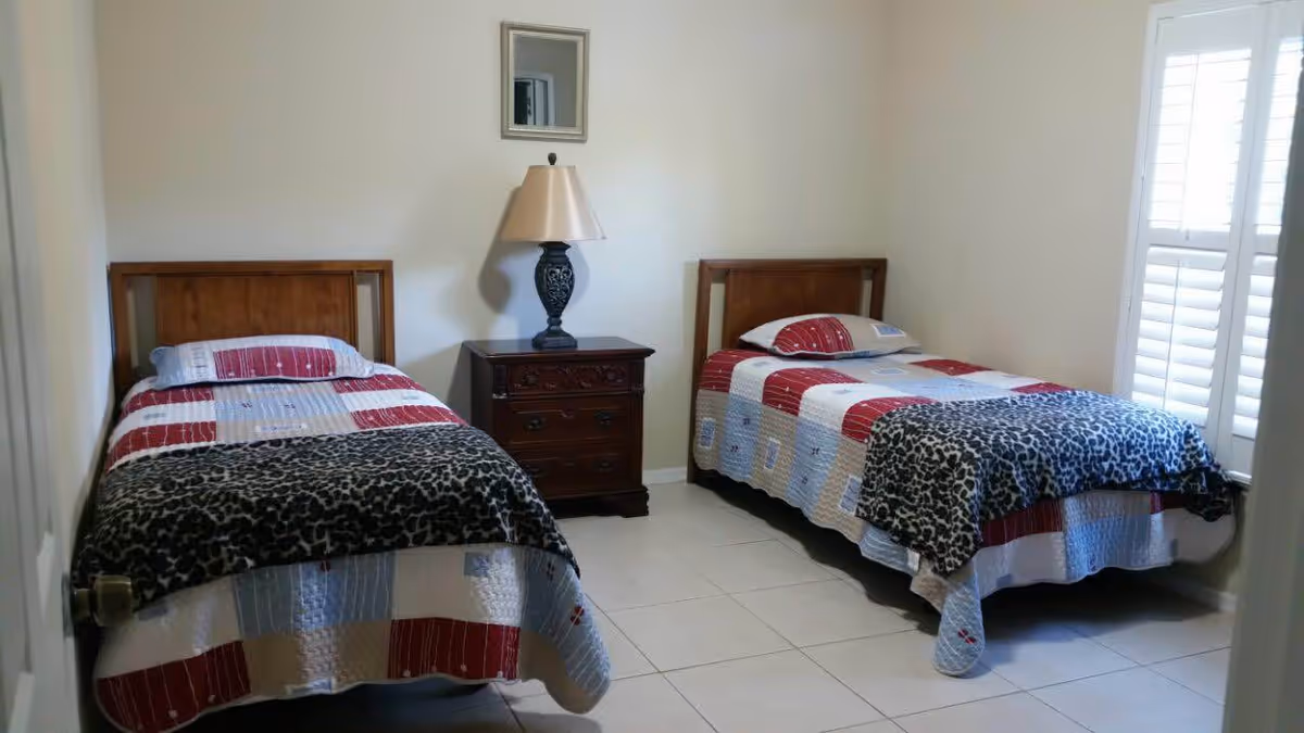 Twin bedroom with two single beds, a wooden nightstand with a lamp between them and a small mirror on the wall, plus a shuttered window.