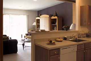 Open kitchen with a countertop and sink overlooking a living room with sofa and a sliding glass door.