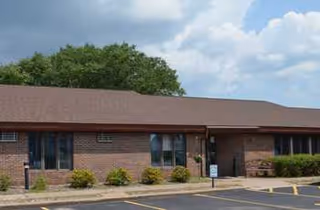 Brick one-story building with windows, shrubs, and a parking lot in front.