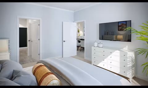 Bright bedroom with a neatly made bed, white dresser topped by a wall-mounted TV, and open doors leading to adjacent rooms.