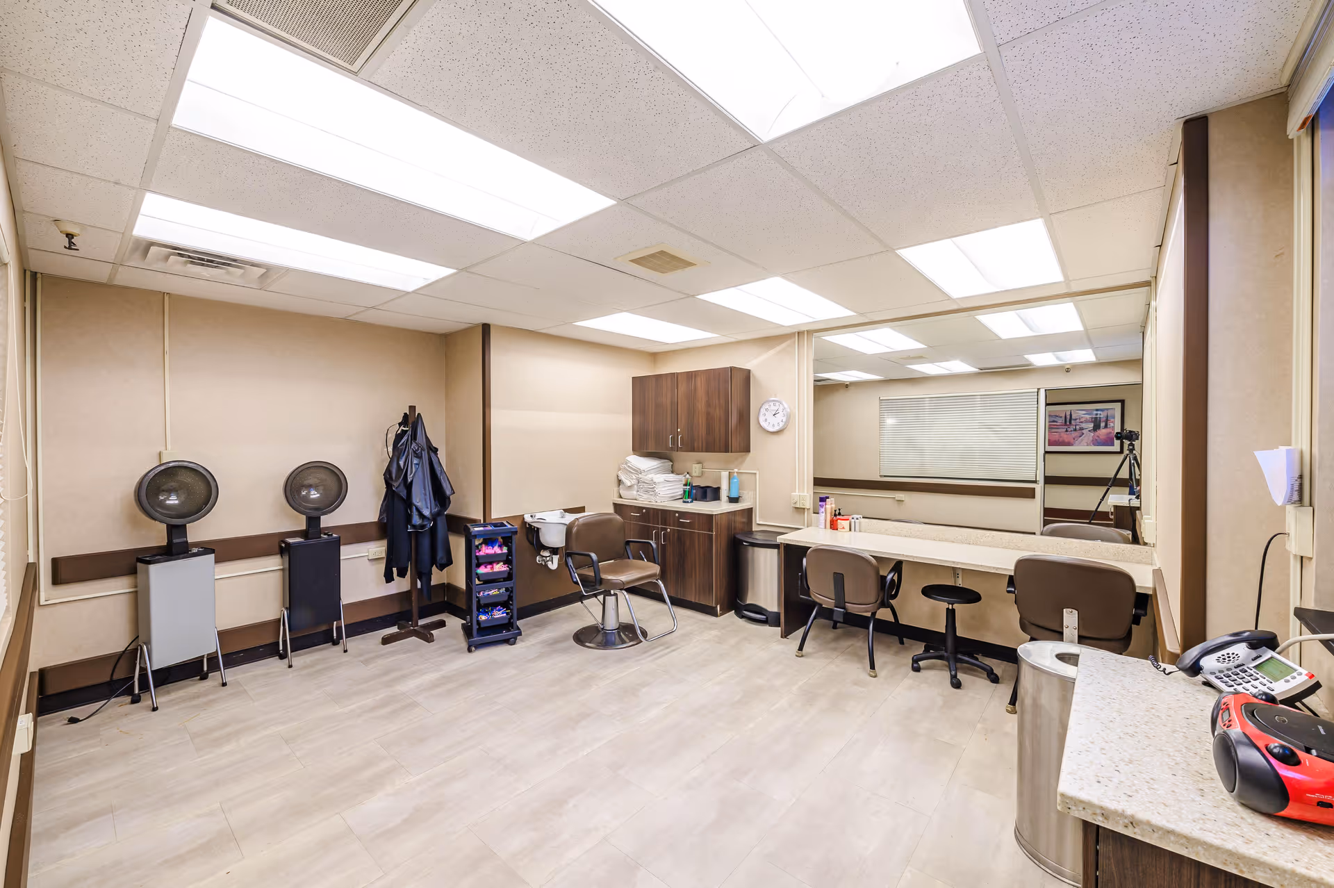 Bright salon-style room with hairdryers, styling chairs, mirrors, cabinets, and workstations in a senior facility.
