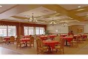 Spacious dining room with round tables covered in red tablecloths, upholstered chairs, chandeliers, and large windows with drapes.