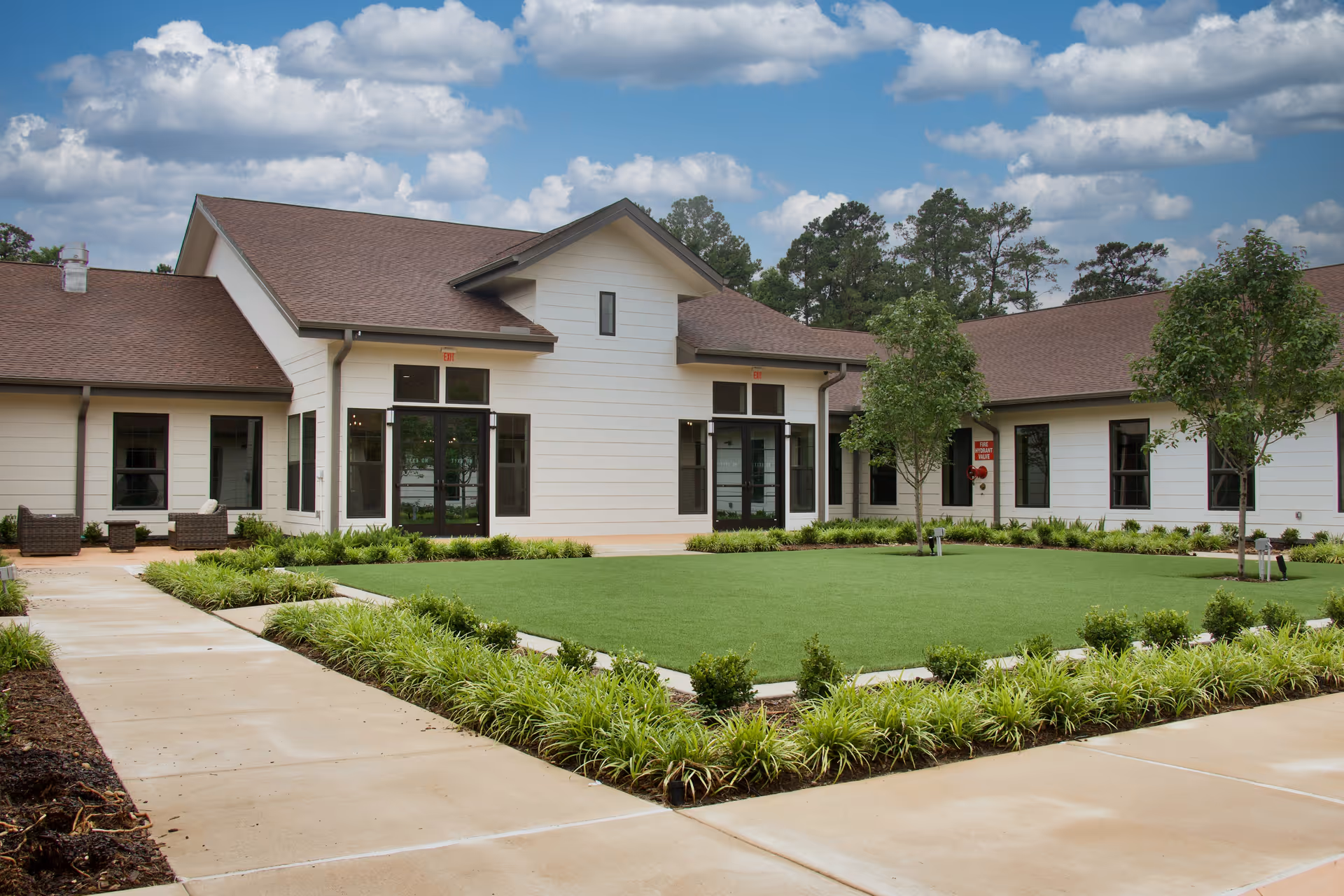 Single-story senior living building with a central glass entrance, manicured lawn and surrounding walkways.