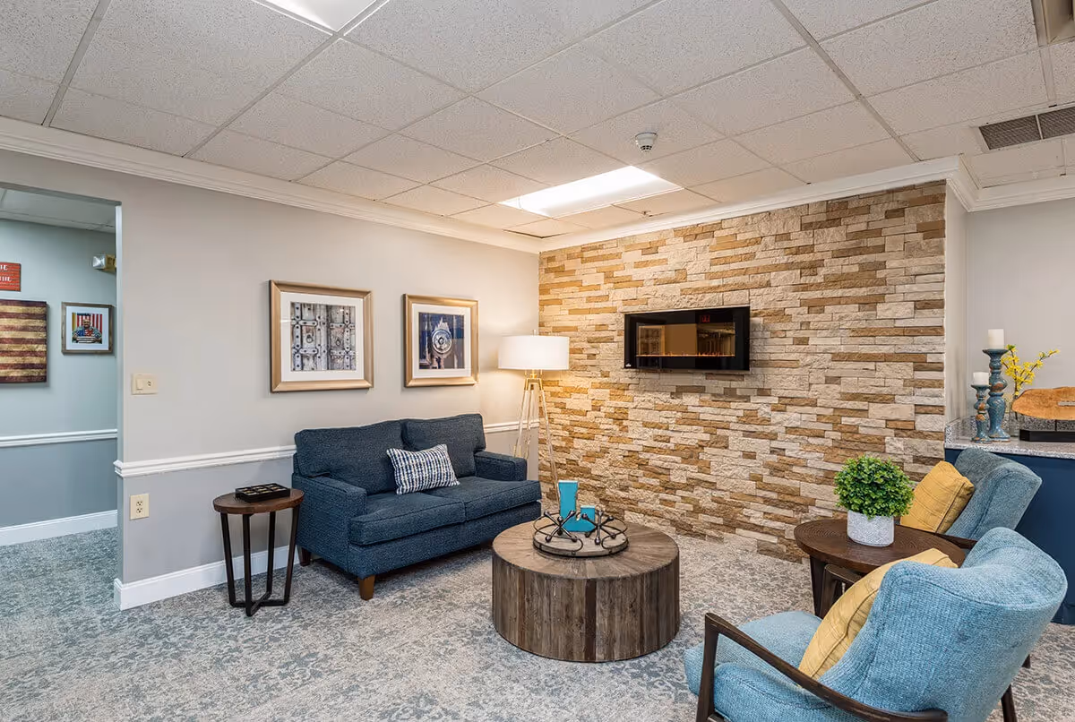 Cozy lounge with a sofa and armchairs around a round wooden coffee table facing a wall-mounted TV on a stone accent wall.