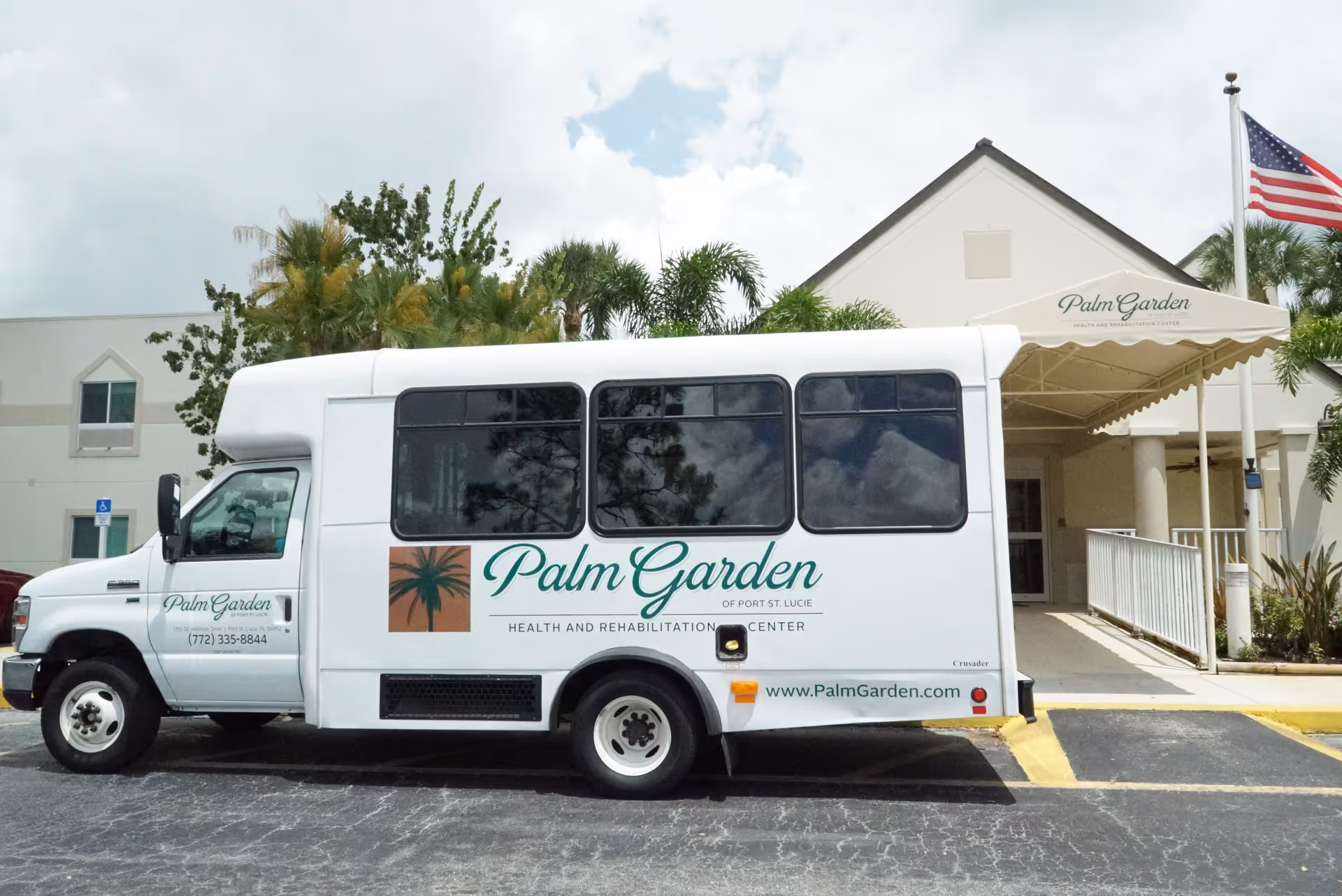 A Palm Garden shuttle van parked in front of the Palm Garden building entrance with a canopy and an American flag.