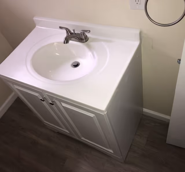 White bathroom vanity with sink, faucet, and towel ring in a compact room.
