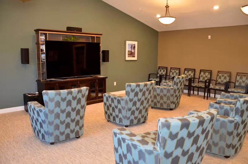 Seating area with patterned armchairs arranged facing a large flat-screen TV in a communal lounge.