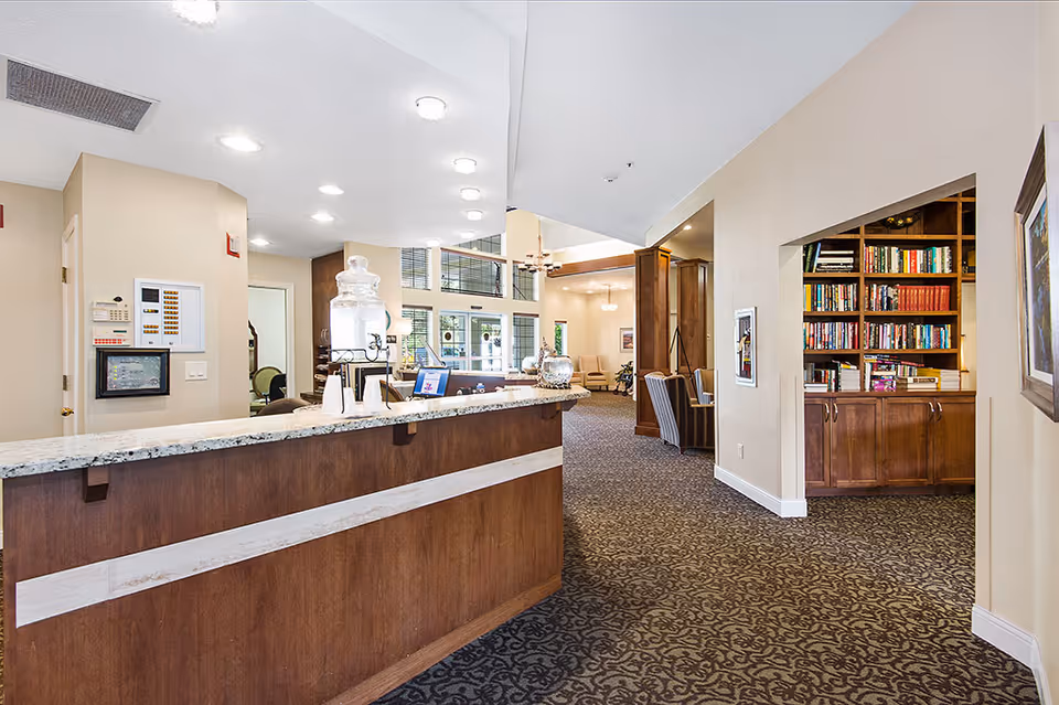 Reception desk and lobby area with a granite countertop, bookshelves, and seating in an assisted living facility.