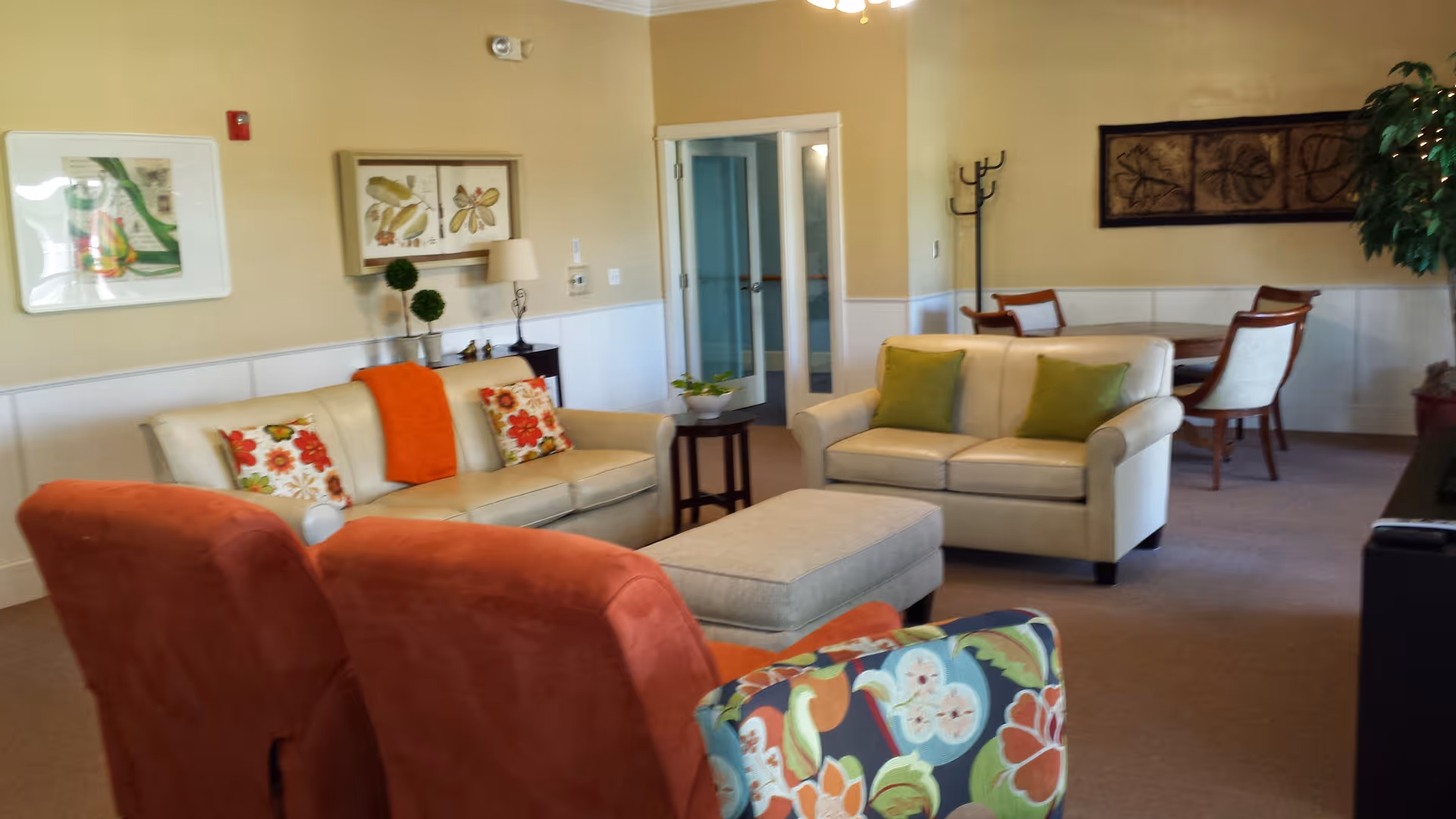 Bright furnished common living room with sofas, armchairs, an ottoman, and a small dining table in the background.