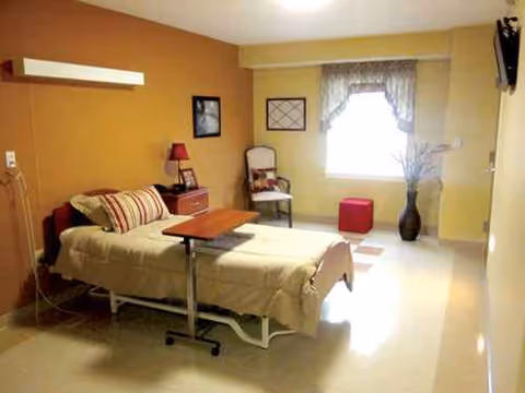 Senior living facility bedroom with a bed, chair, dresser, and window with curtains.