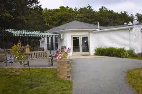 White single-story facility with front door, outdoor seating, and American flags near steps.