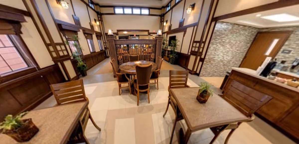 Communal dining area with wooden tables and chairs, wood-paneled walls, potted plants, and a service counter.