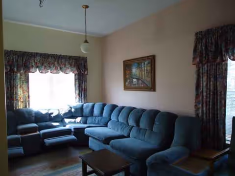 Blue sectional sofa fills a cozy living room with floral curtains and wall art.