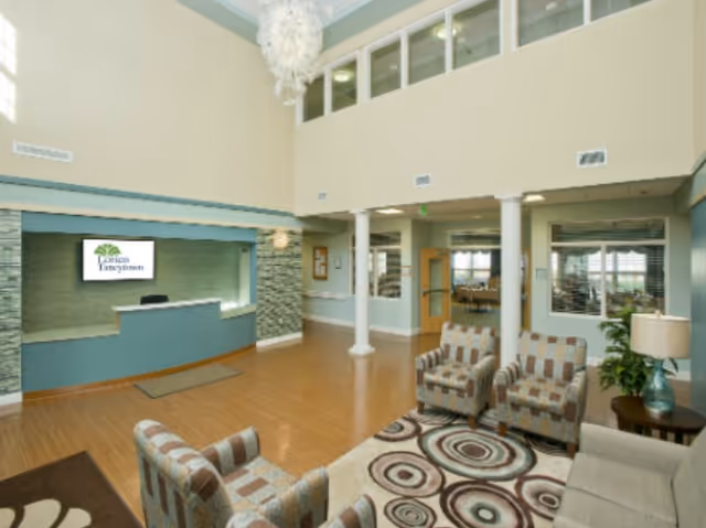 Spacious senior living lobby with a reception desk, seating area, patterned rug and high ceilings.