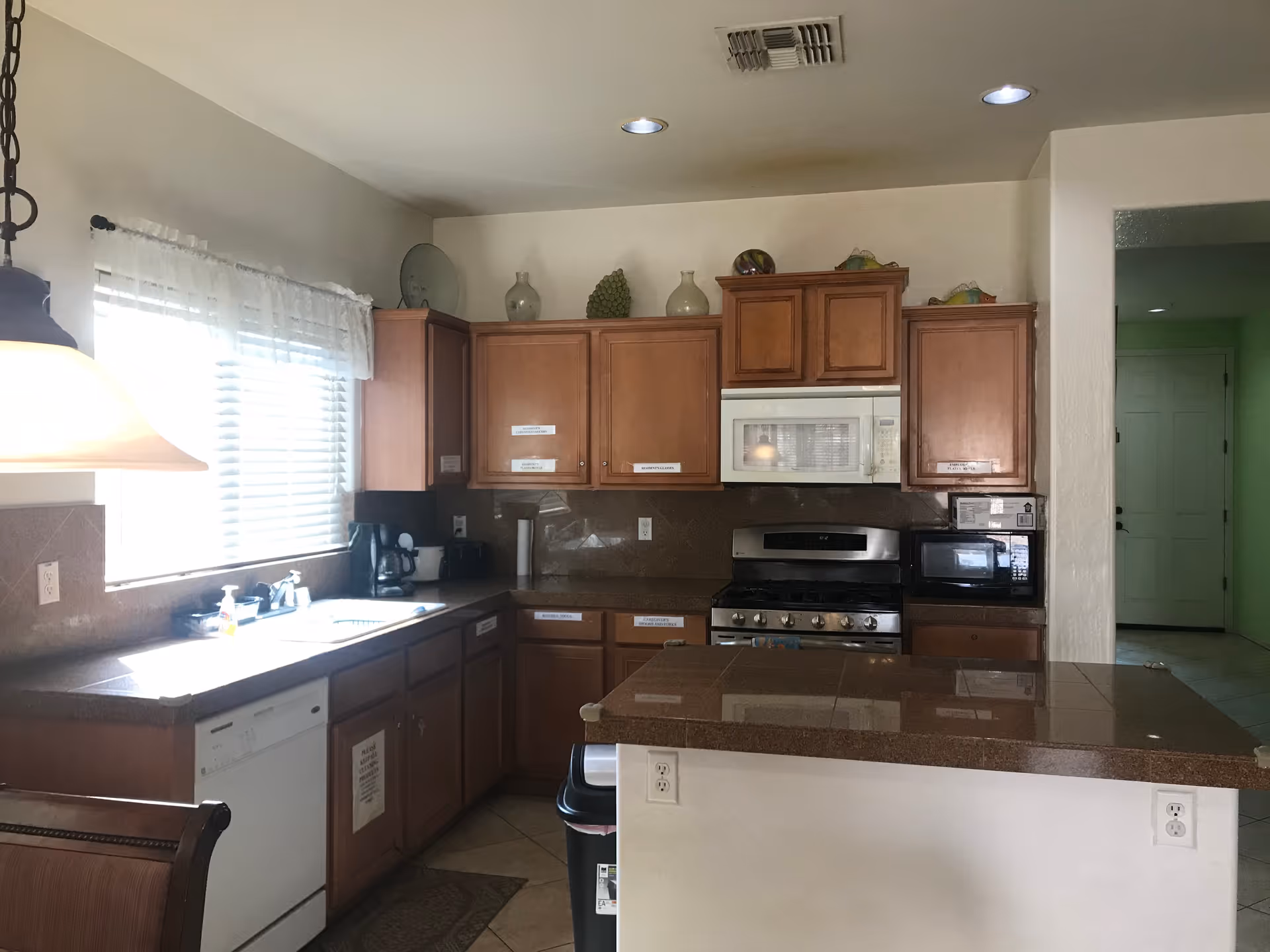 Bright kitchen with wooden cabinets, a center island and countertop, stainless steel stove and microwave, dishwasher, and a window with blinds.