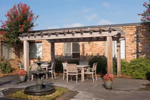 Outdoor patio with a wooden pergola, seating table set, fountain, potted plants, brick building.