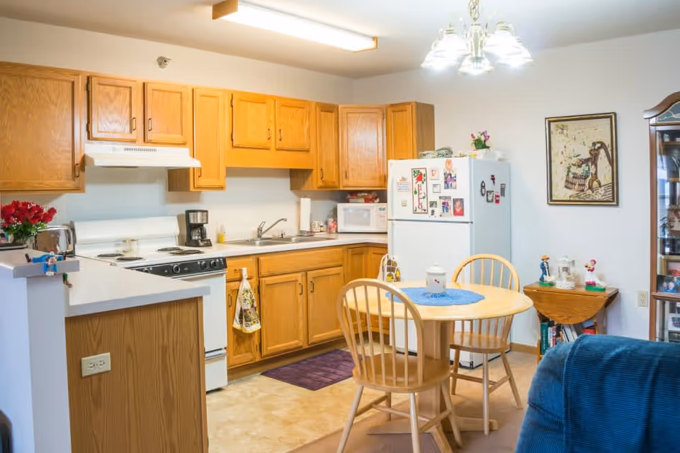 Cozy kitchen and dining area with oak cabinets, white stove and refrigerator, and a round wooden table with chairs.