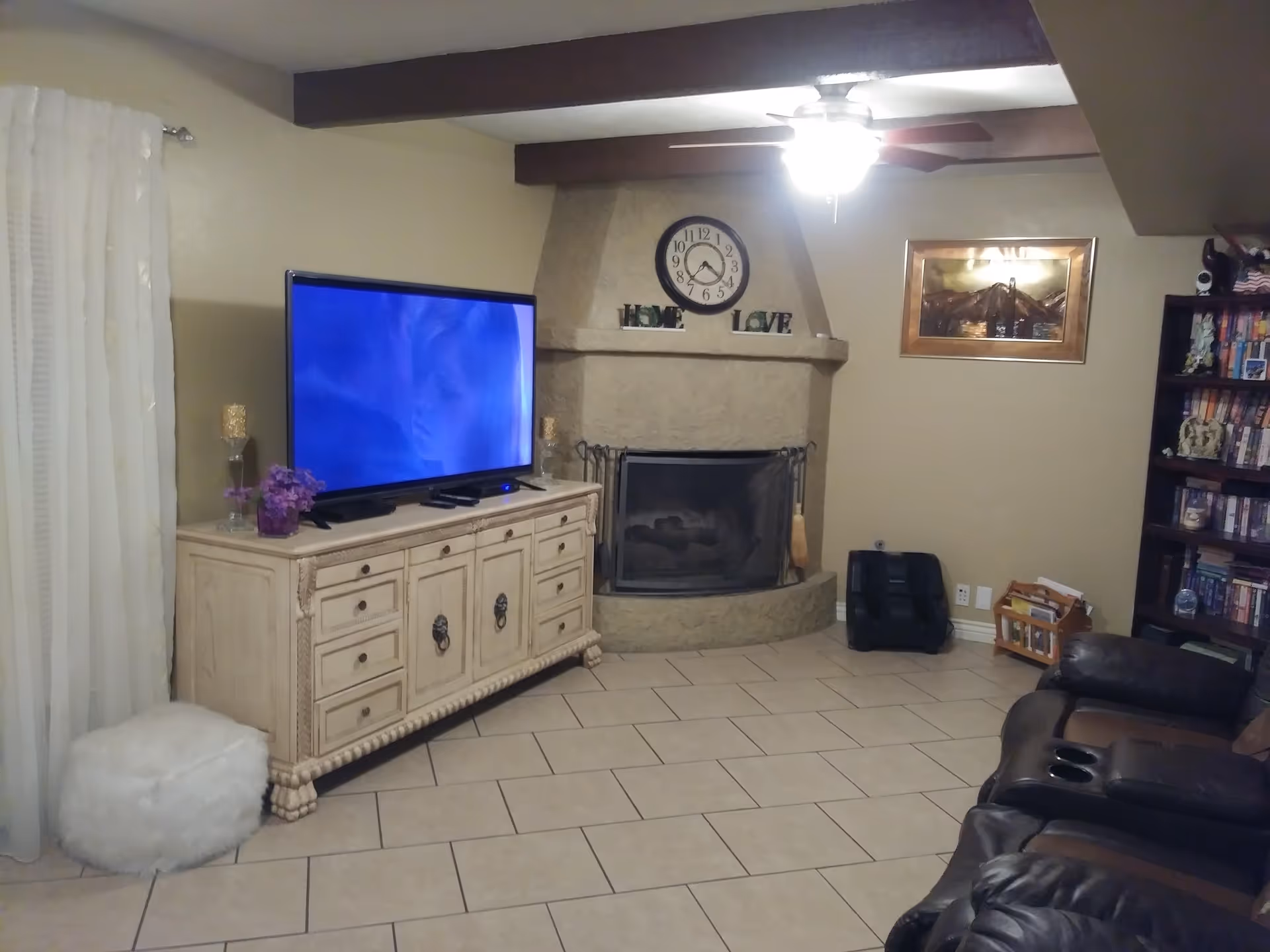 Cozy living room with a large TV on a wooden console, a stone fireplace, leather recliners and a bookshelf.