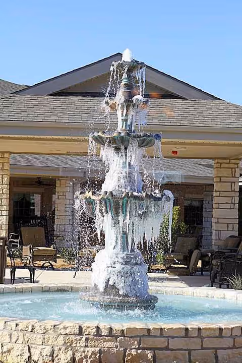 Multi-tier fountain in a courtyard with seating, in front of a stone building entrance.