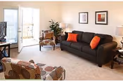 Cozy senior apartment living room with sofa, armchairs, plants, and wall art.