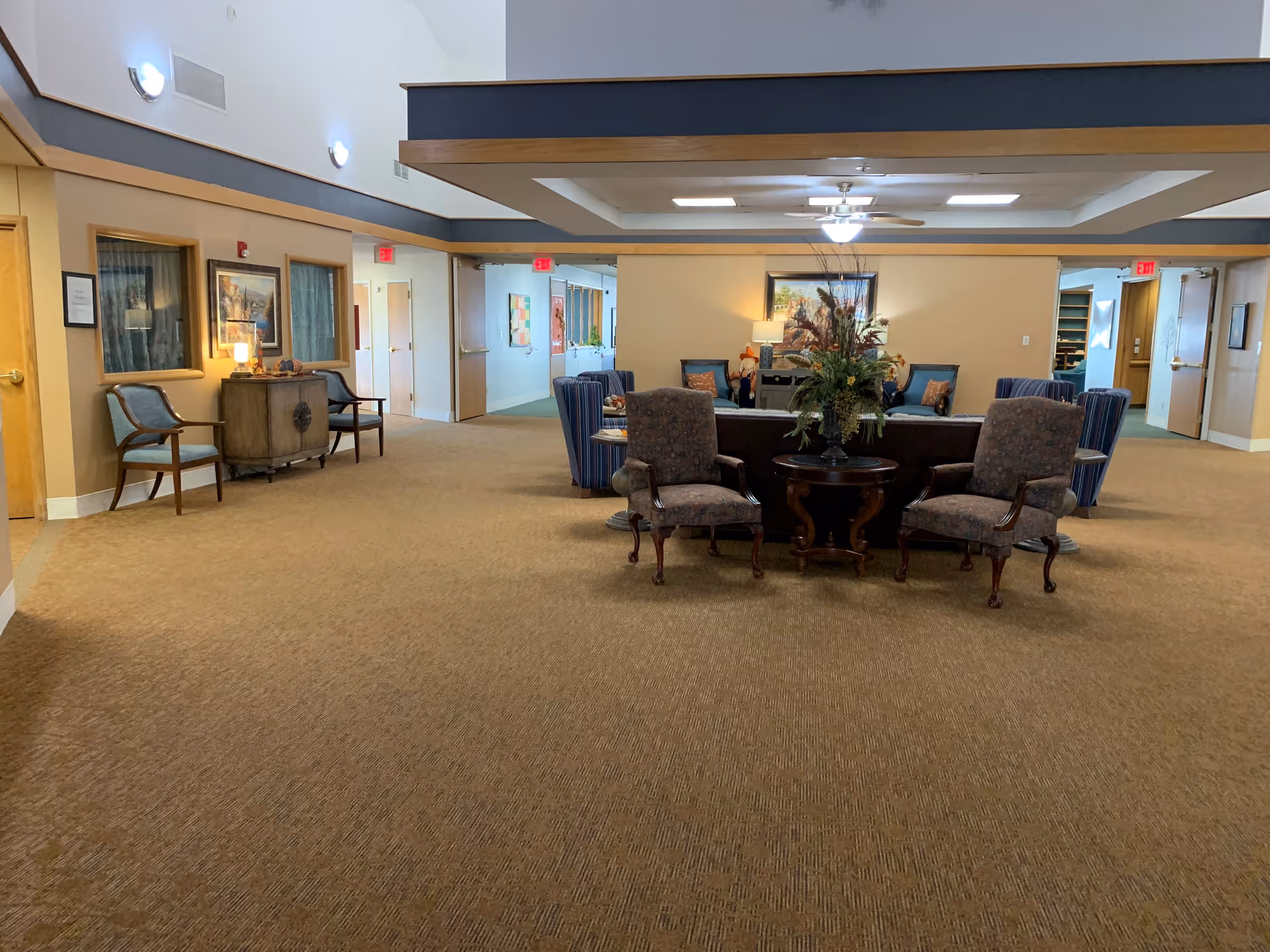 A spacious lobby area featuring comfortable seating, decorative plants, and artwork on the walls, with doors leading to other rooms.