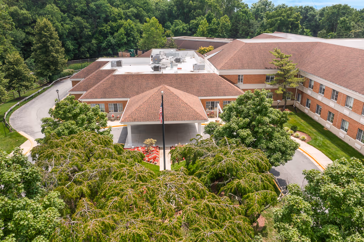 Aerial view of a brick senior living facility with a covered entrance canopy, circular driveway, and surrounding trees.