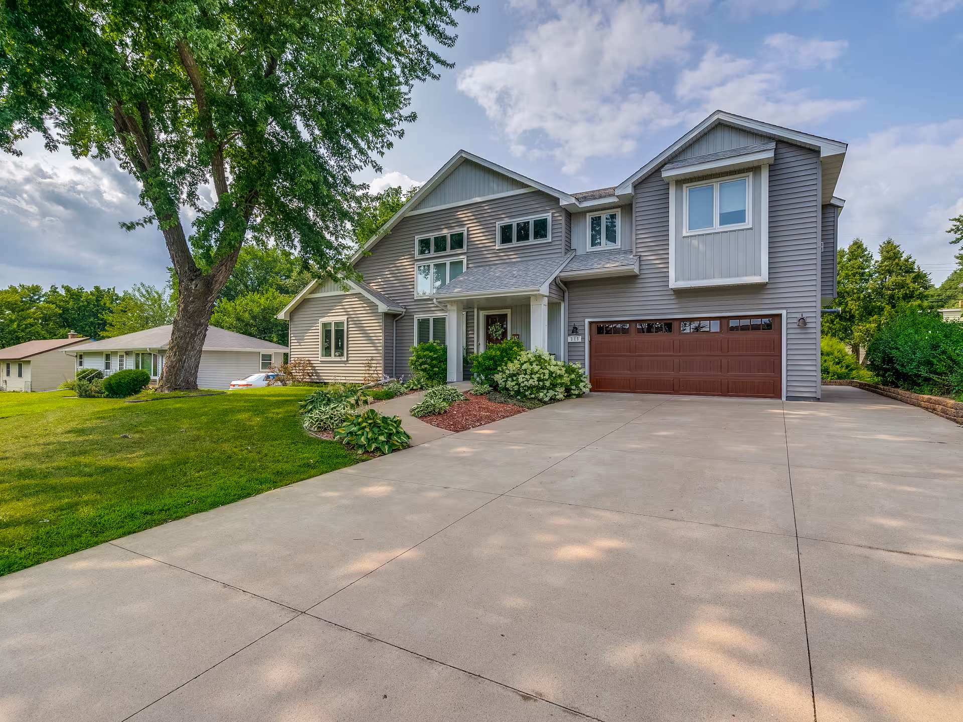 Front exterior of a two-story suburban house with a large driveway, attached garage, and landscaped yard.