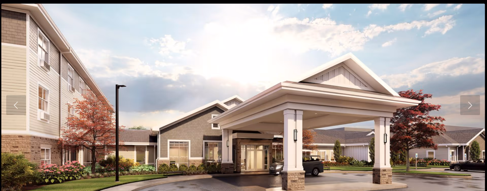 Exterior front entrance of a senior living facility with a covered porte-cochère, cars, and landscaped grounds.