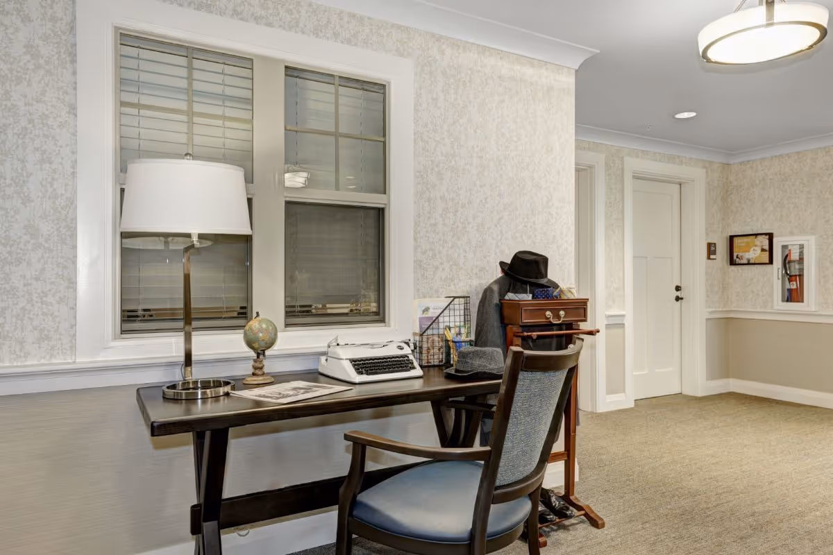 A cozy interior desk area with a lamp, vintage typewriter, small globe and chair along a hallway.
