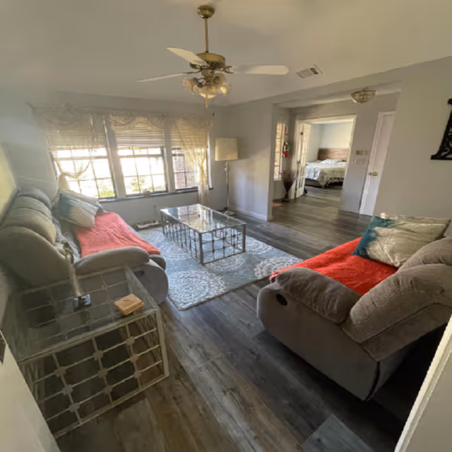 Cozy living room with two couches, glass coffee table, rug, and large window blinds.