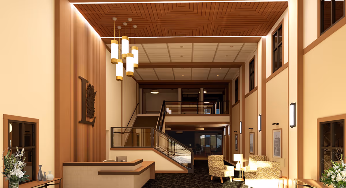 Bright two-story lobby with a reception desk, seating area, and central staircase beneath a high ceiling and hanging lights.