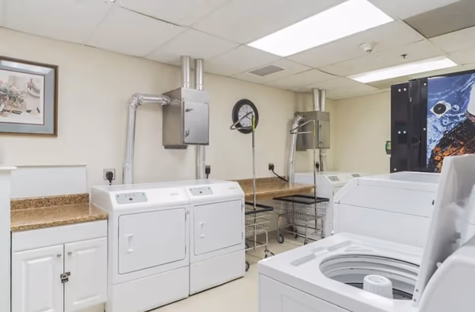 Communal laundry room with several washers and dryers, folding counters, and laundry carts.