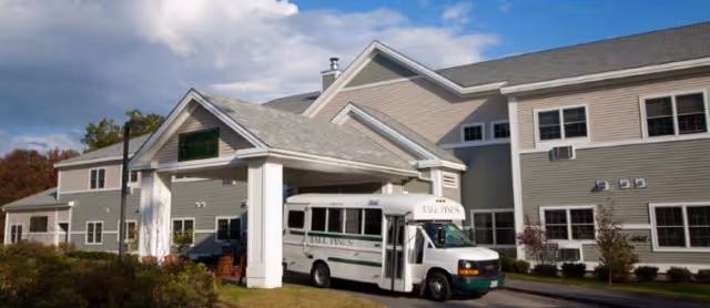 Front view of the Tall Pines Community building with a covered entrance and a white shuttle bus parked underneath.