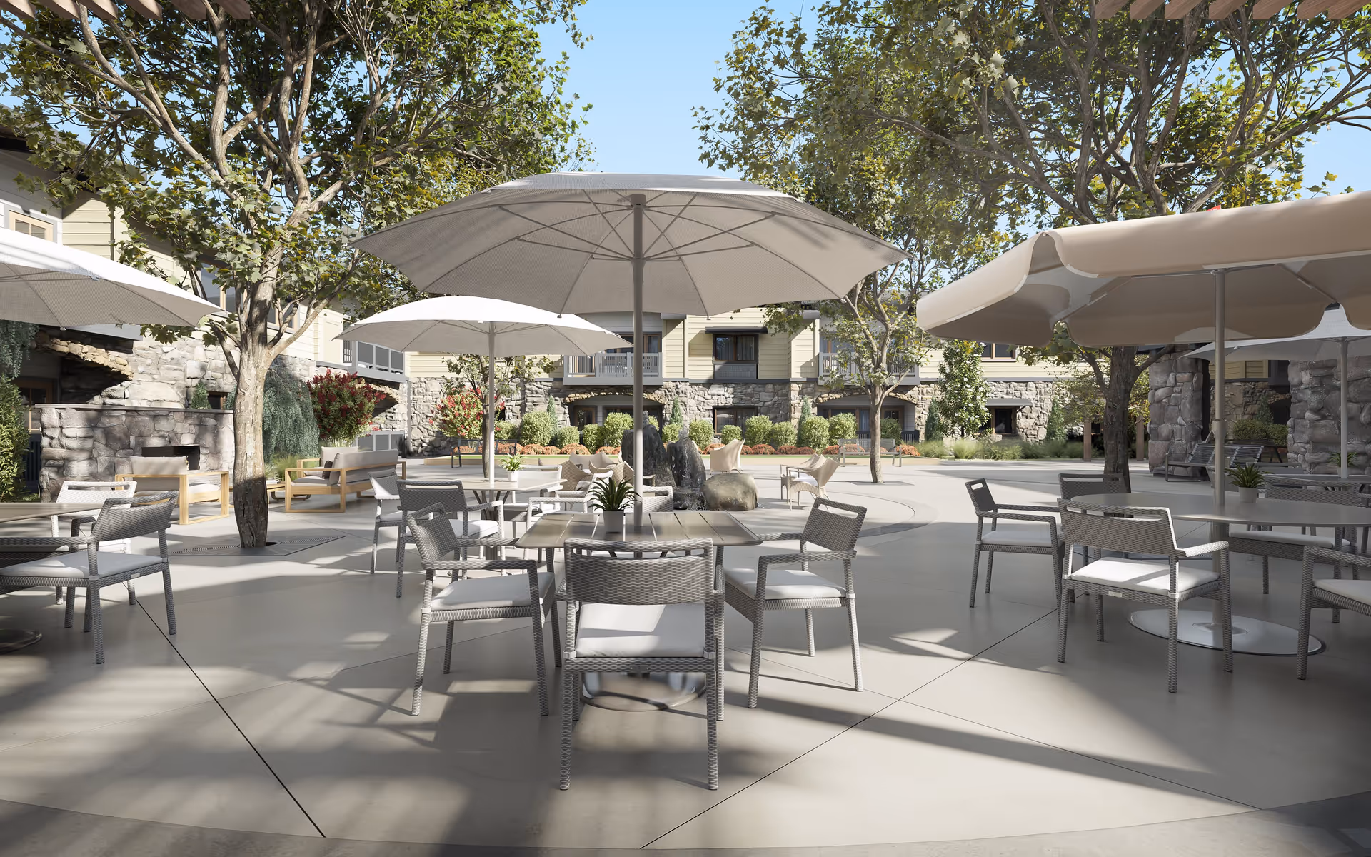 Outdoor courtyard with tables, chairs, and large umbrellas surrounded by trees and a stone-faced senior residence building.