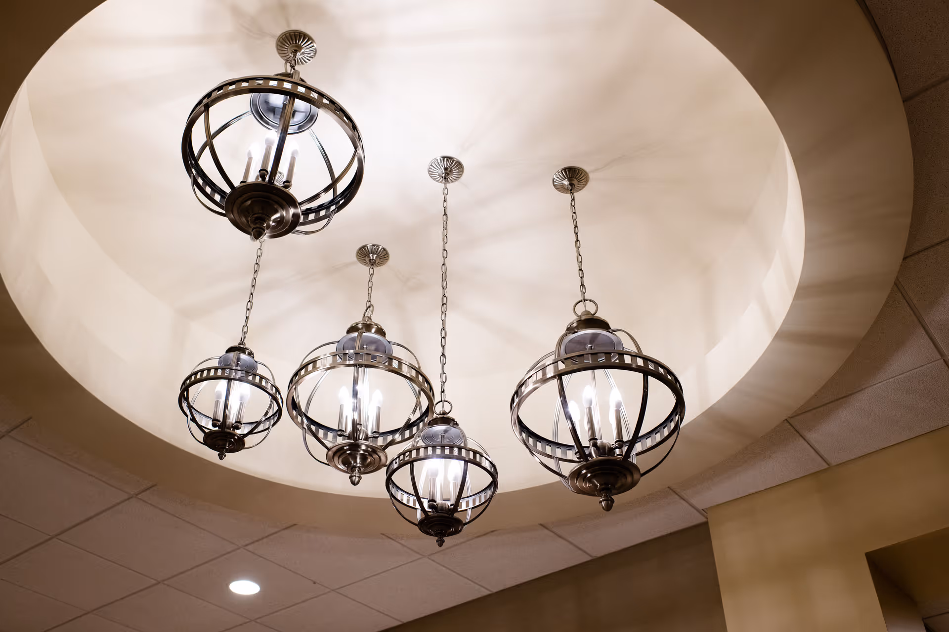 Five decorative pendant lights with metal frames hanging from the ceiling inside a circular recessed area, casting shadows on the ceiling.