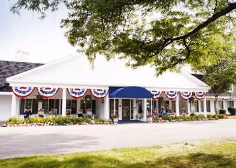 Front of American House Dearborn Heights senior living facility with bunting and outdoor seating.