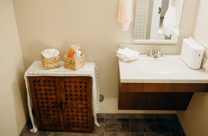 Bathroom vanity with sink, mirror, and a wooden cabinet topped with woven baskets and towels.