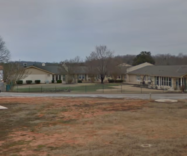Single-story senior living facility buildings surrounding a grassy courtyard under a cloudy sky.