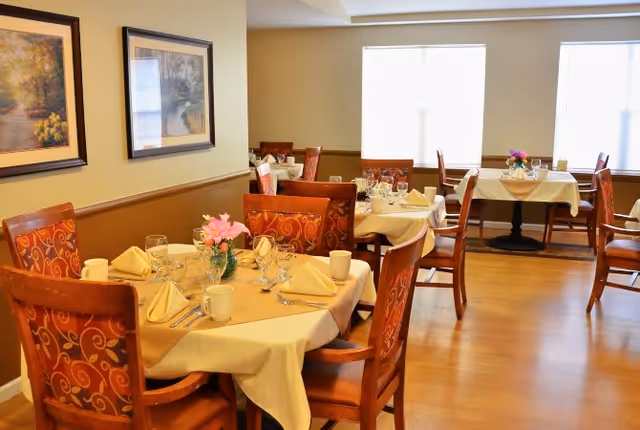 A well-lit dining room with multiple tables set with plates, glassware, napkins, and floral centerpieces.