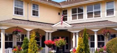 Front entrance of a Brookdale Monroe senior living facility with arched porch and hanging plants.