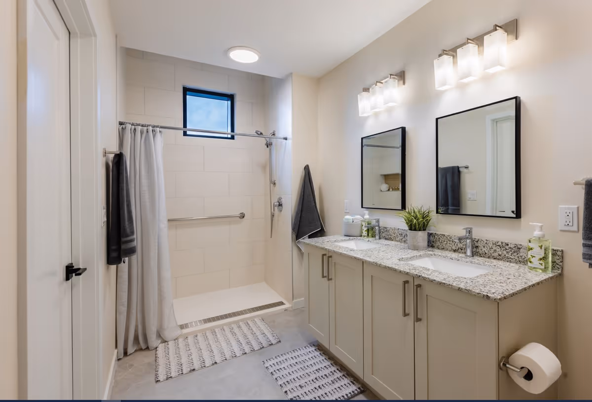 Bright modern bathroom with a double-sink vanity, two mirrors, and a walk-in shower with a curtain.