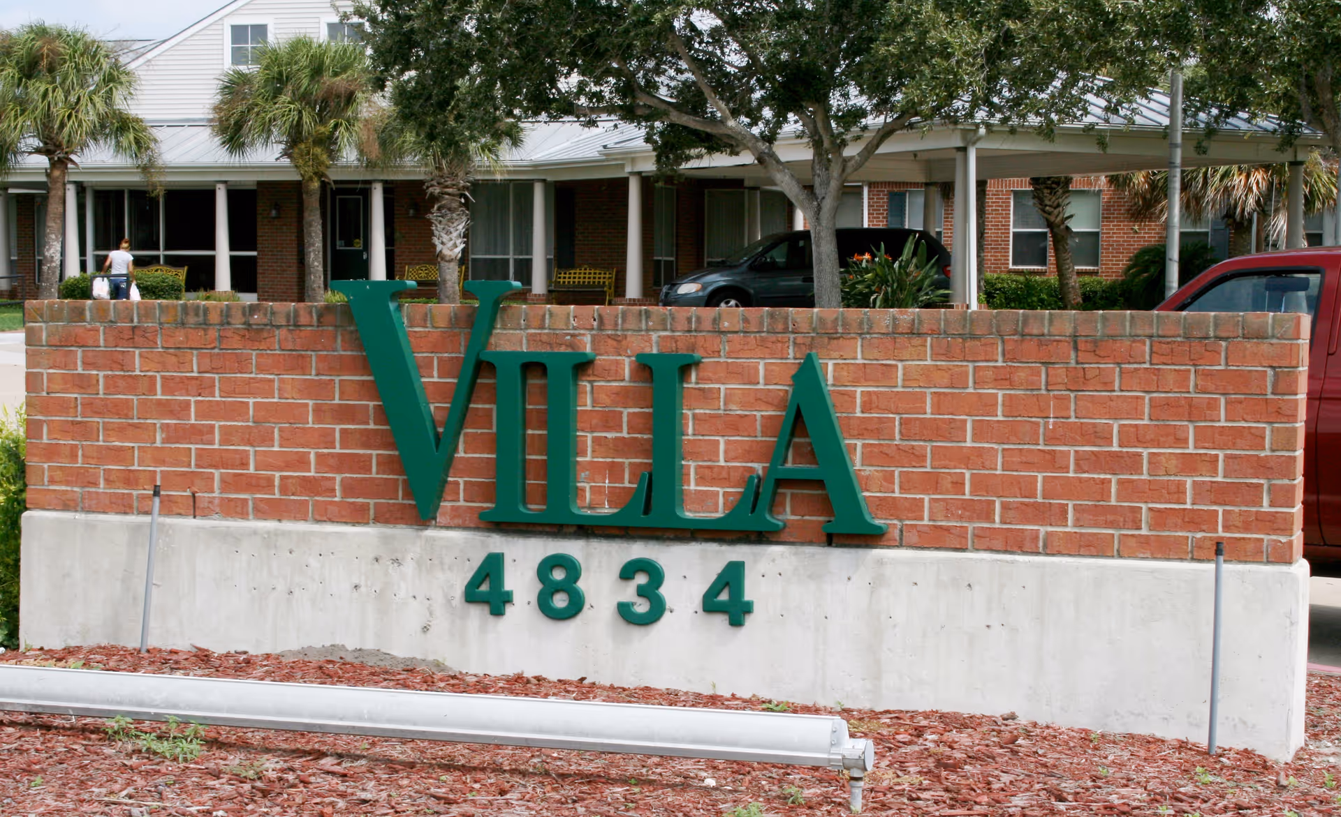 Brick entrance sign reading 'VILLA' with address '4834' mounted on a low wall in front of a single-story building and landscaping.