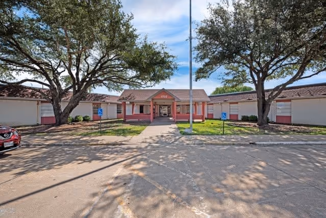 Front exterior view of Golden Grace Day Activity and Health Services building with a central entrance, two large trees on either side, and a parking area with handicap parking signs.