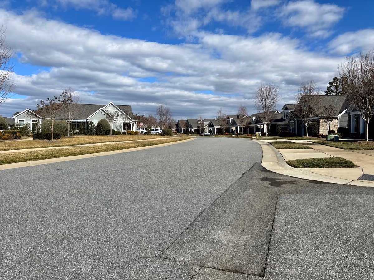 Wide view down a quiet street lined with single-story homes and lawns under a partly cloudy sky.