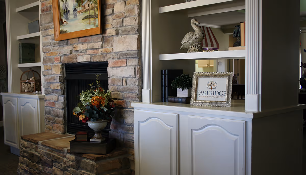 Interior living area with a stone fireplace flanked by built-in white shelves and cabinets decorated with plants, books and a framed Eastridge sign.