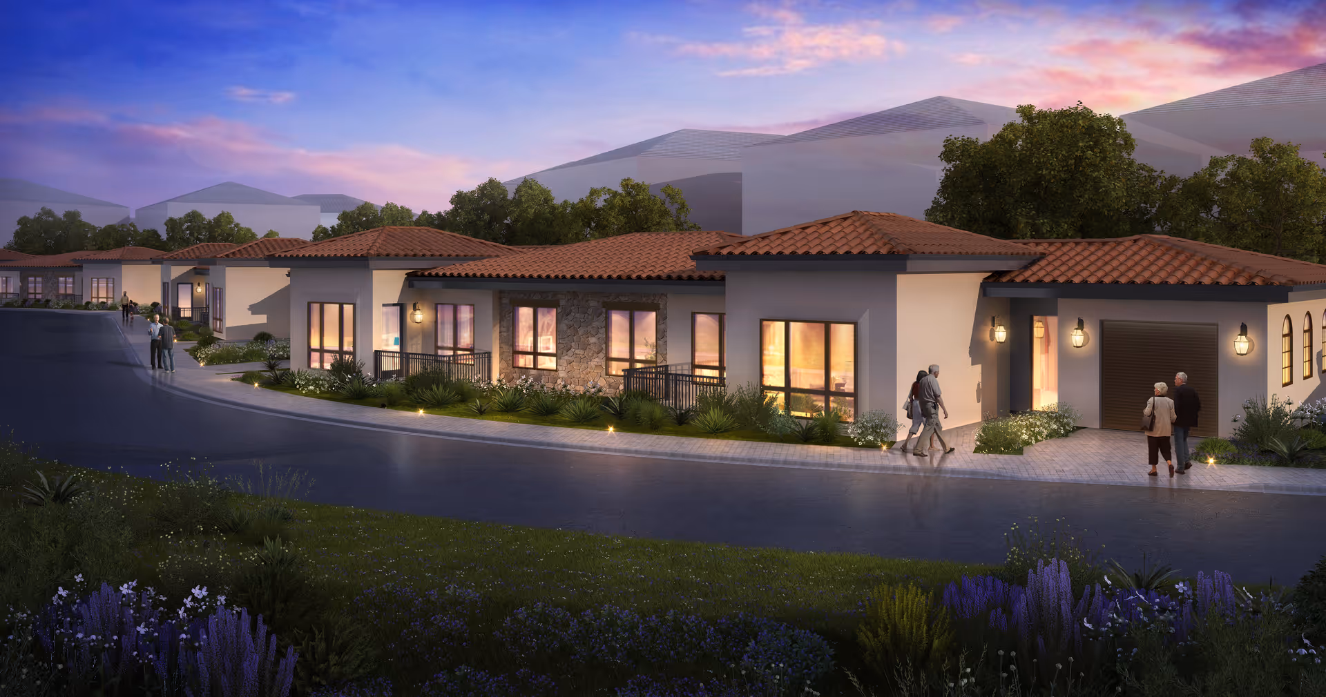 Dusk exterior view of a single-story Mediterranean-style senior living building with lit windows and people walking along the sidewalk.
